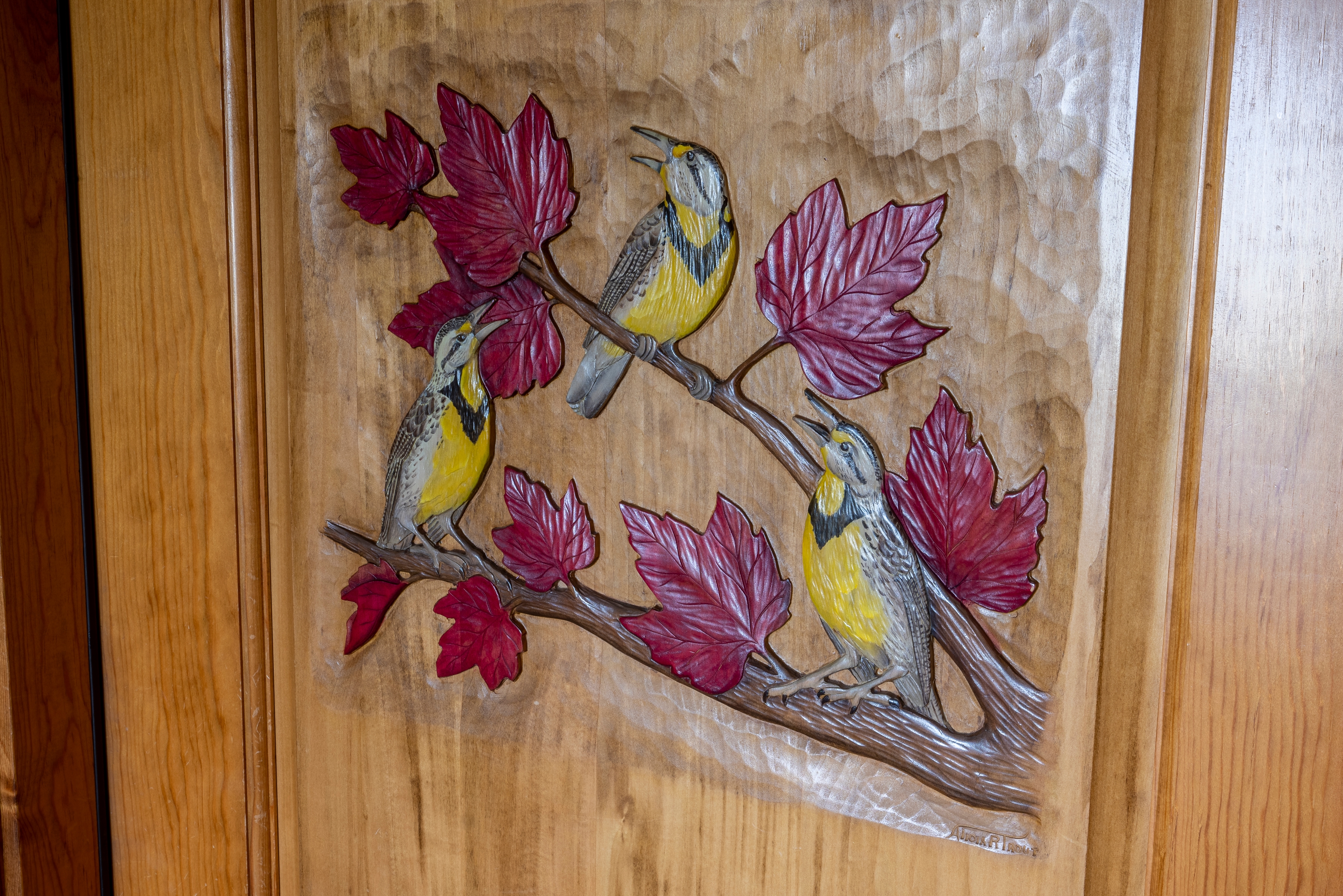 A colorful wood carving of three birds perched on a branch with leaves.