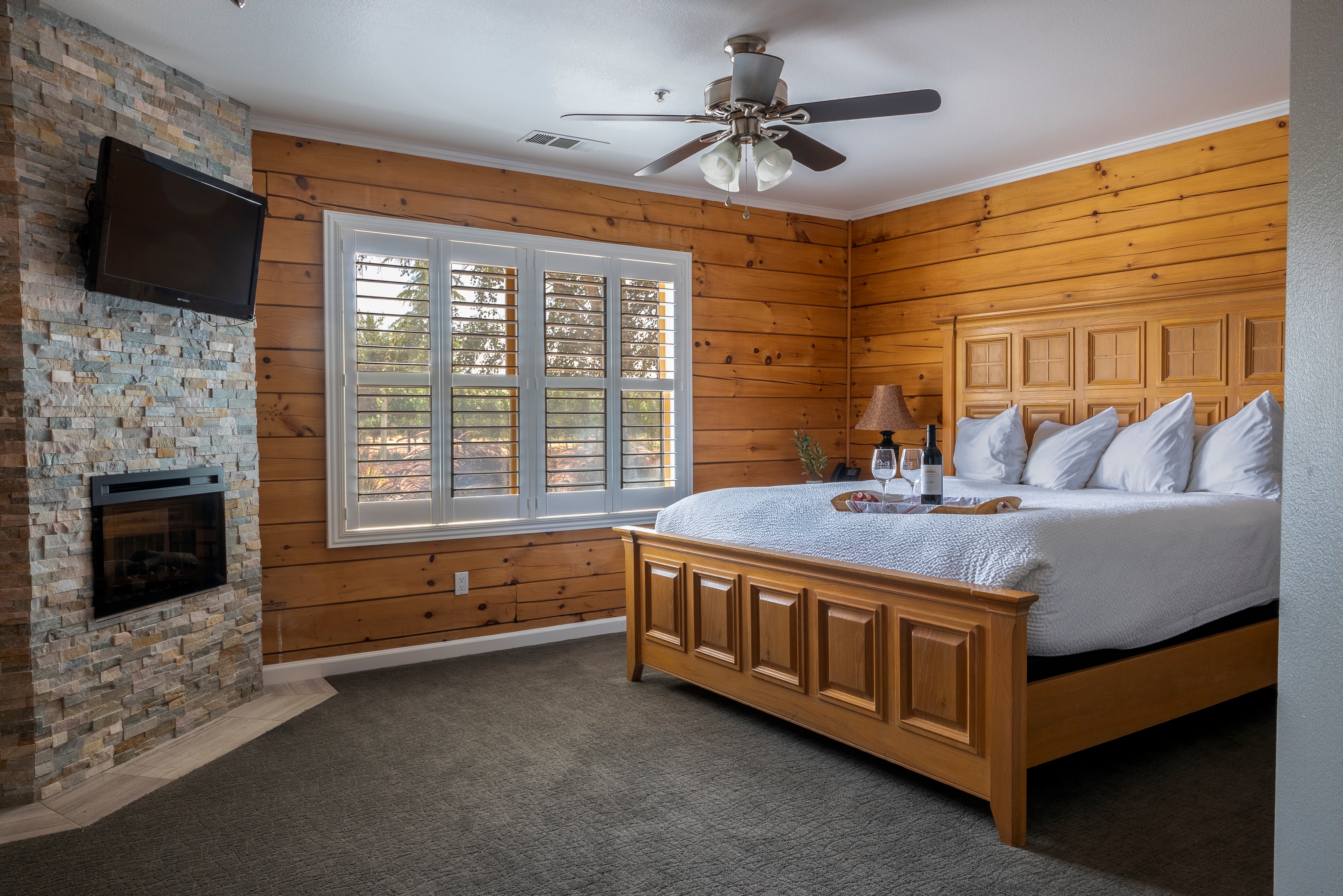 An inviting room with a king-size bed, a fireplace with stone surround, and wooden walls.