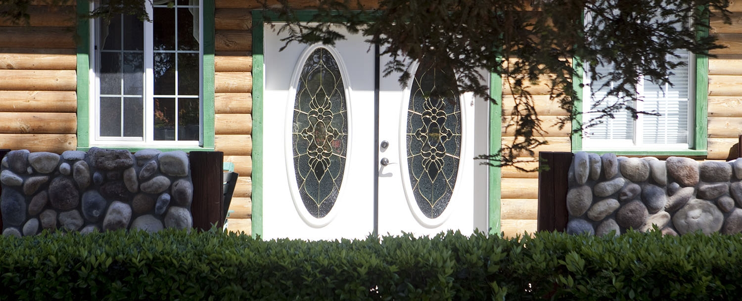 Front entry featuring two white doors with decorative glass panes. The entrance is framed by stonework and a row of bushes.