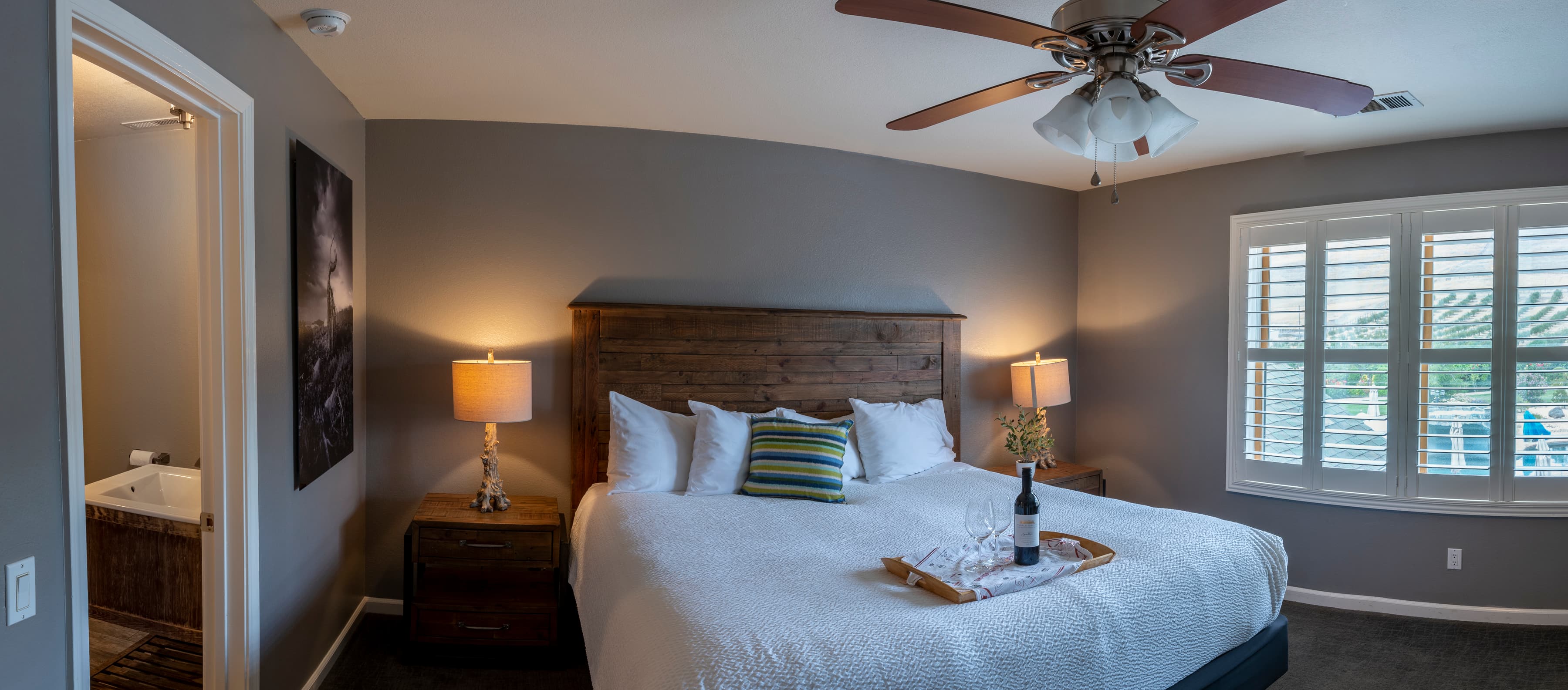A spacious room with a king-size bed, two nightstands, and a ceiling fan. The window overlooks the olive orchard.