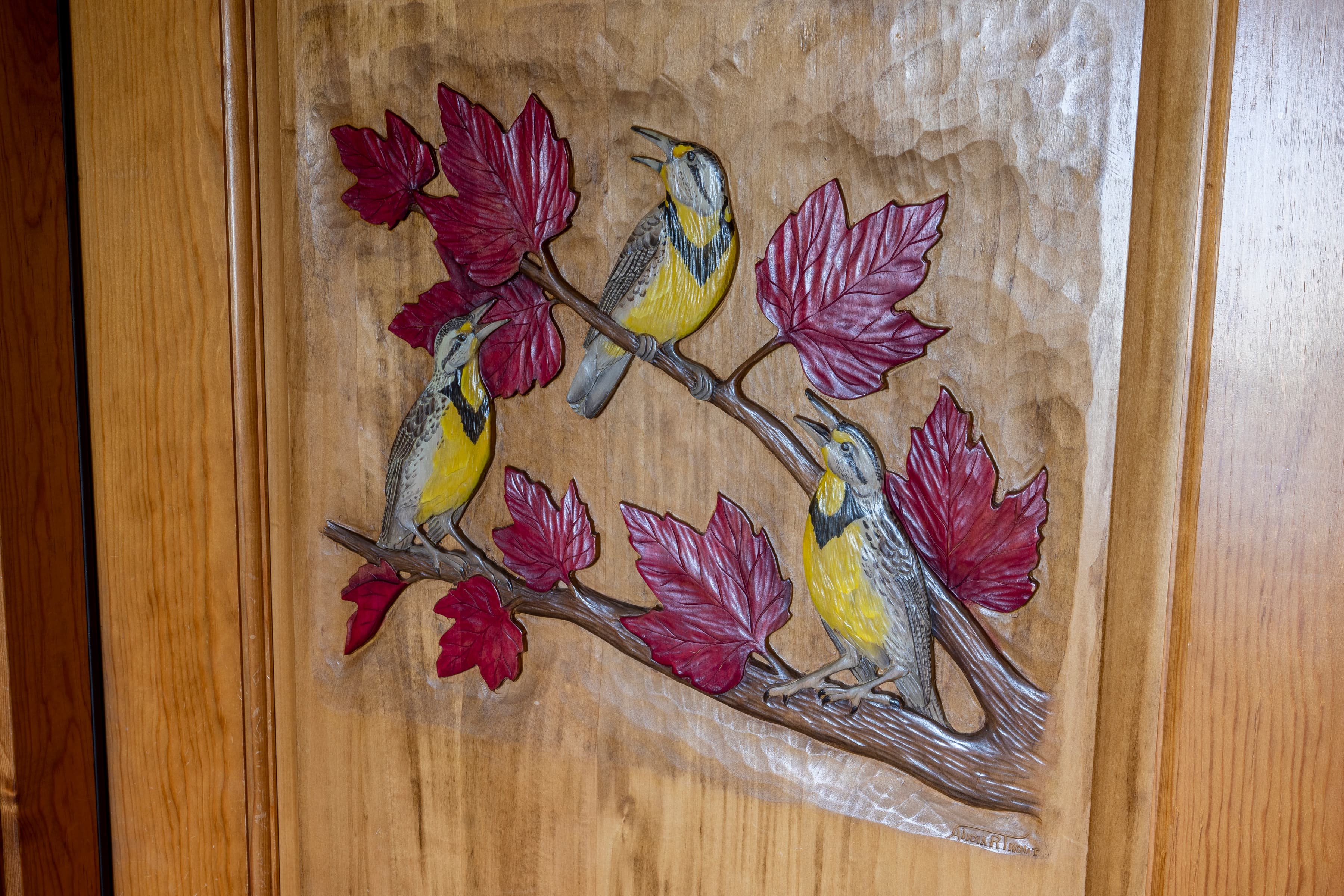 A colorful wood carving of three birds perched on a branch with leaves.