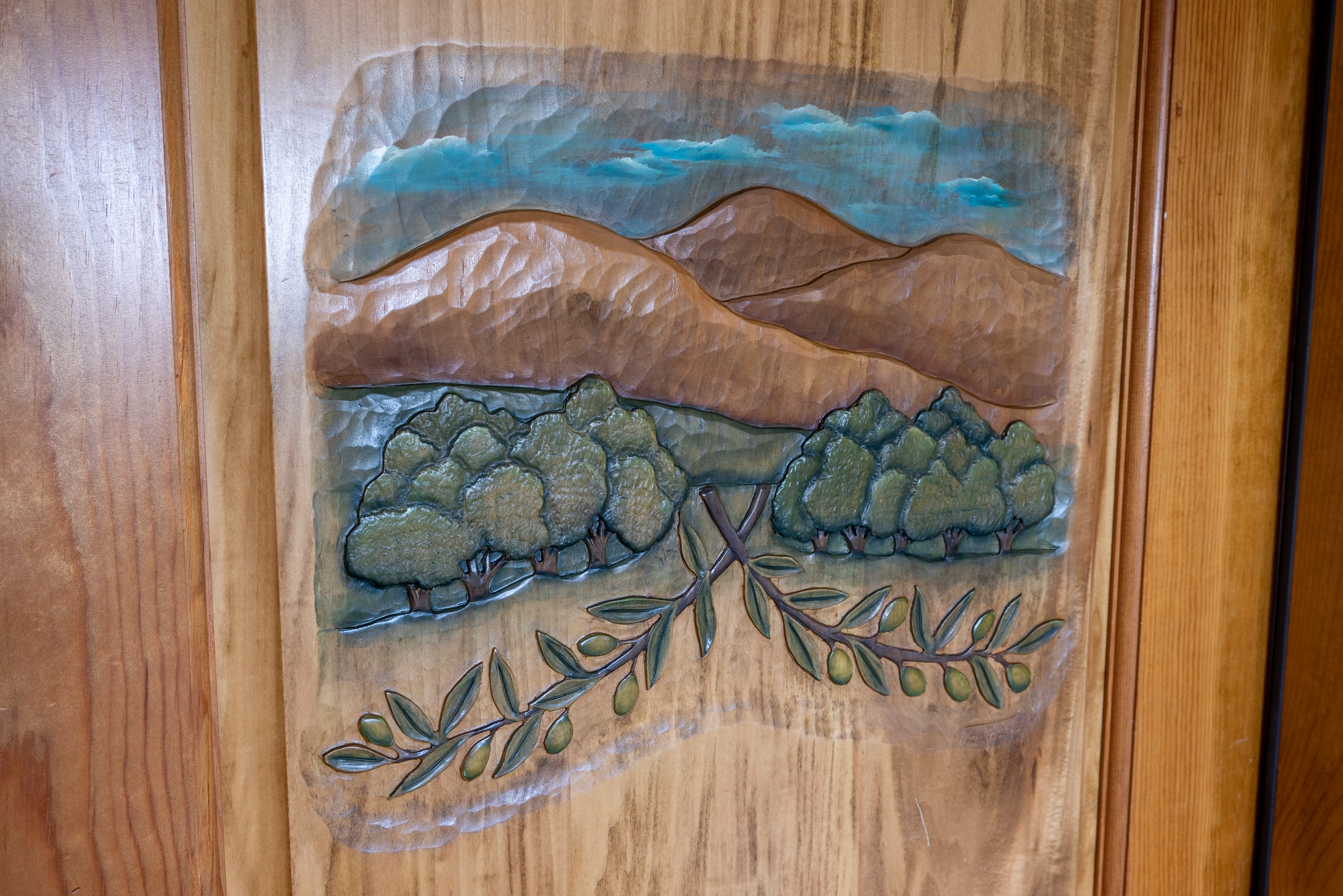 A wood carving of a landscape scene with hills, trees, and an olive branch.