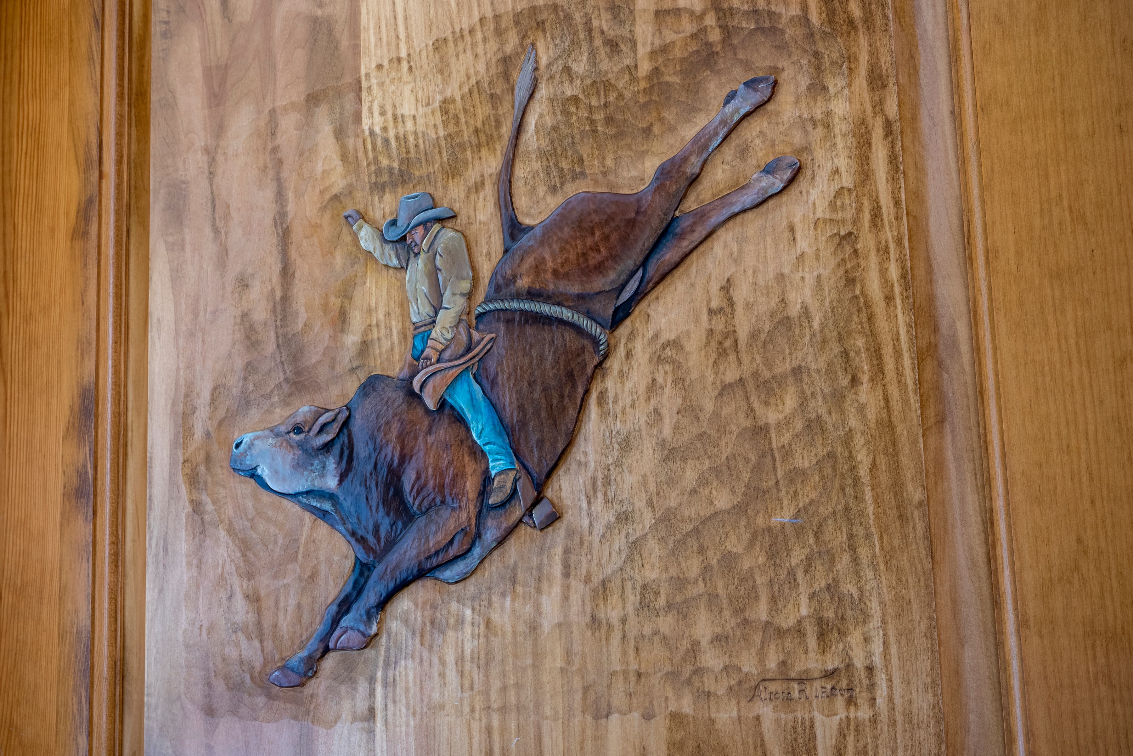 A detailed wood carving depicting a bull rider in a rodeo. The rider is holding on tight as the bull bucks and leaps through the air.