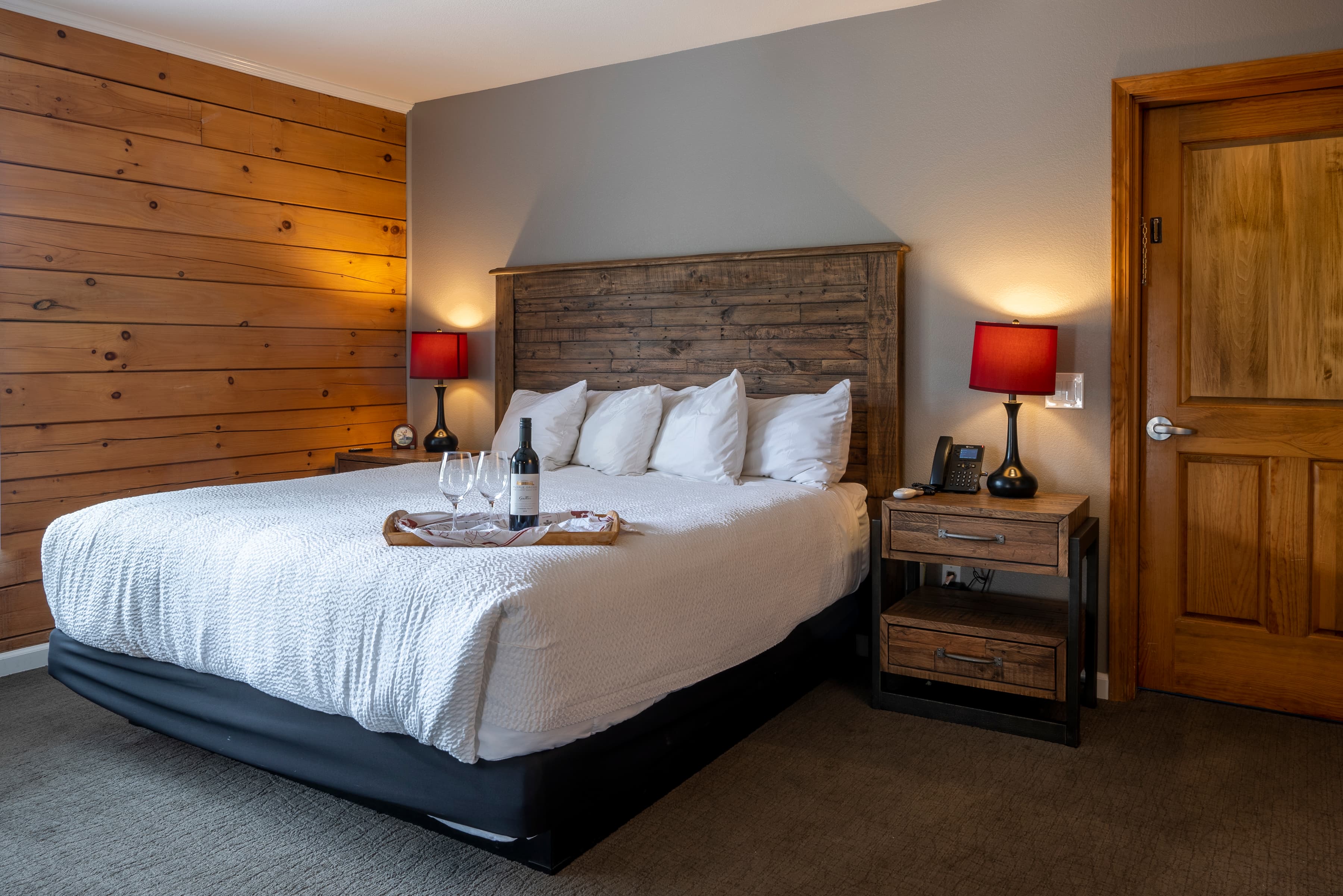 A welcoming room with a king-size bed, wood paneled walls and painted walls, and a tray with a bottle of wine on the bed.