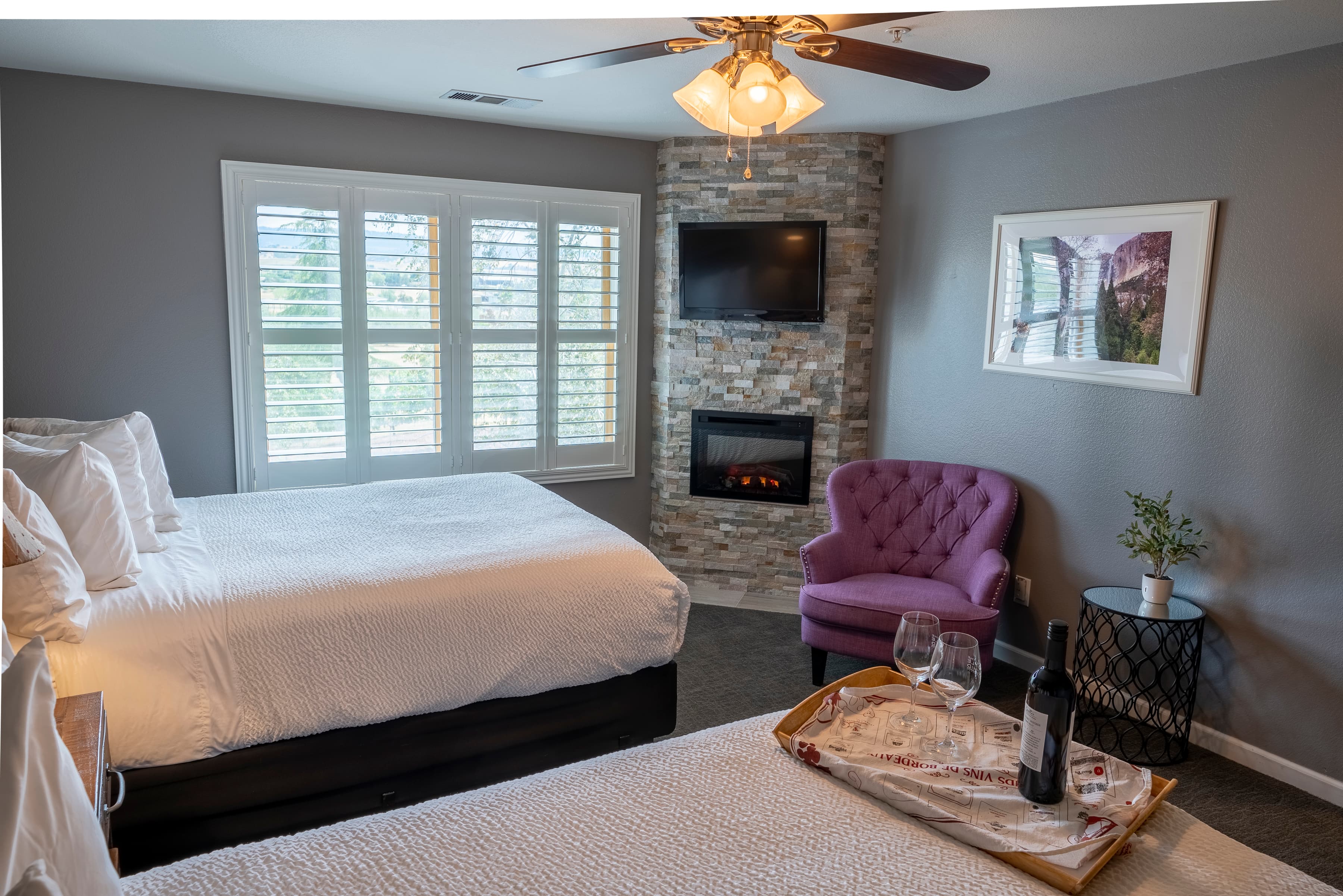 A tranquil room with two queen-size beds, a corner fireplace, a large window, and a purple armchair.
