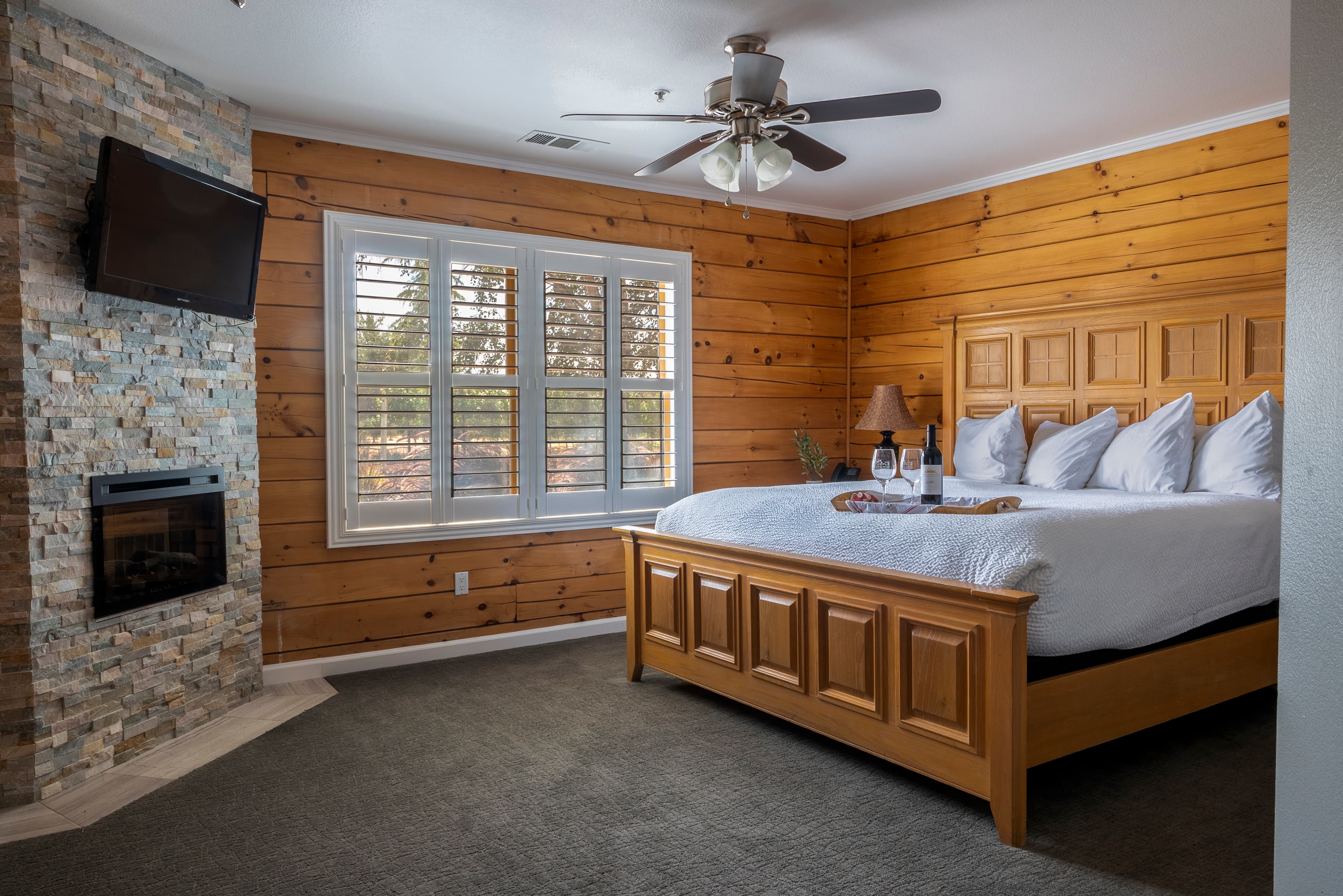 An inviting room with a king-size bed, a fireplace with stone surround, and wooden walls.