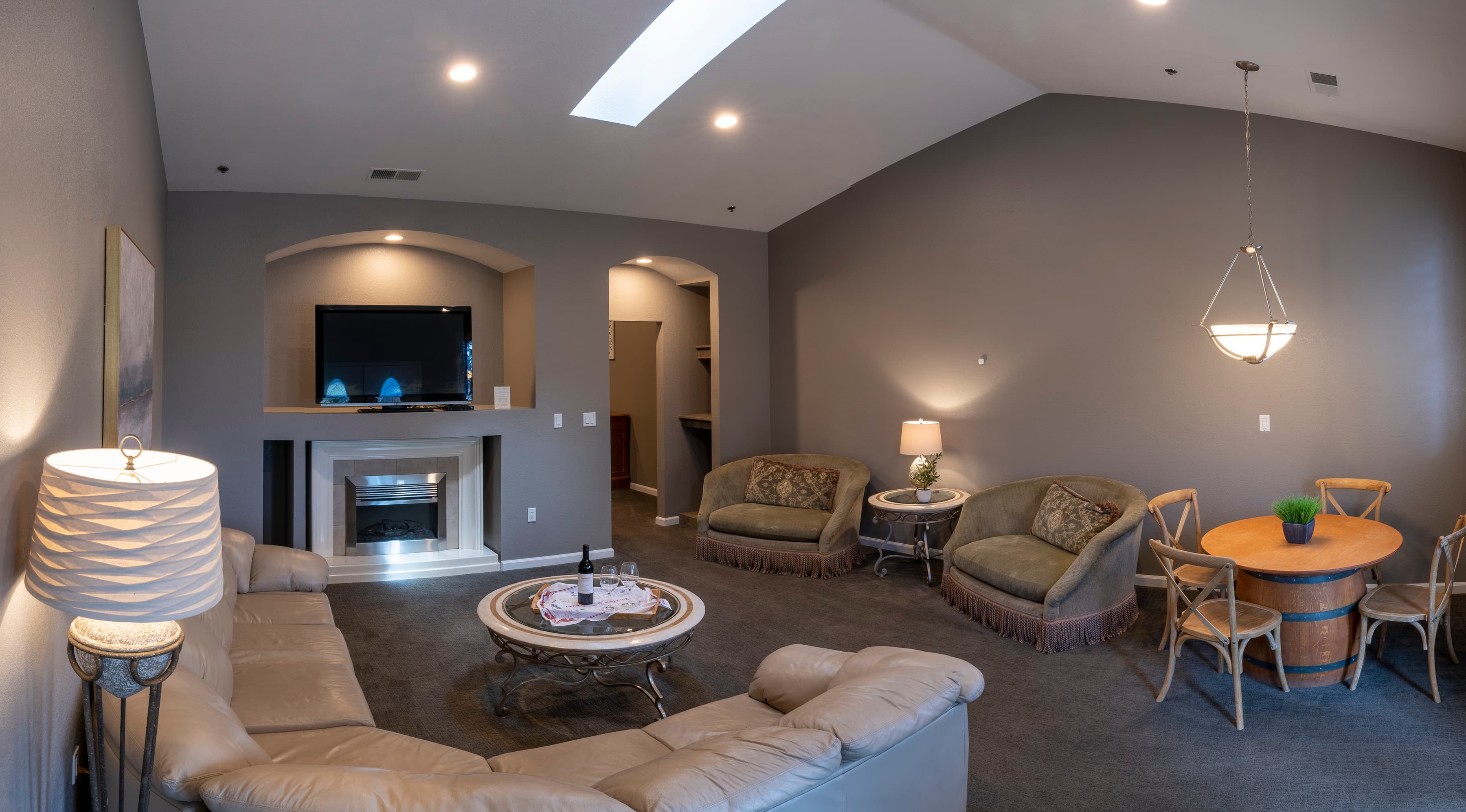 A spacious living room with a fireplace, a flat-screen TV, a dining table with chairs, and comfortable seating area with a sofa and armchairs.