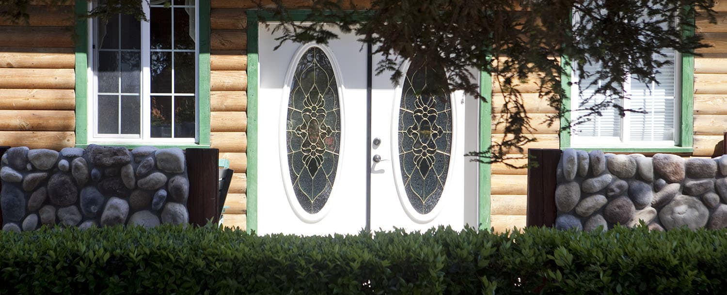 Front entry featuring two white doors with decorative glass panes. The entrance is framed by stonework and a row of bushes.