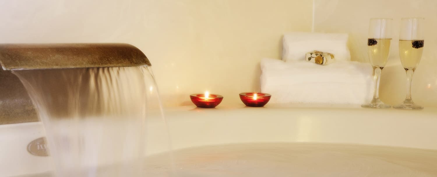 A bathtub with running water, candles, and champagne glasses.