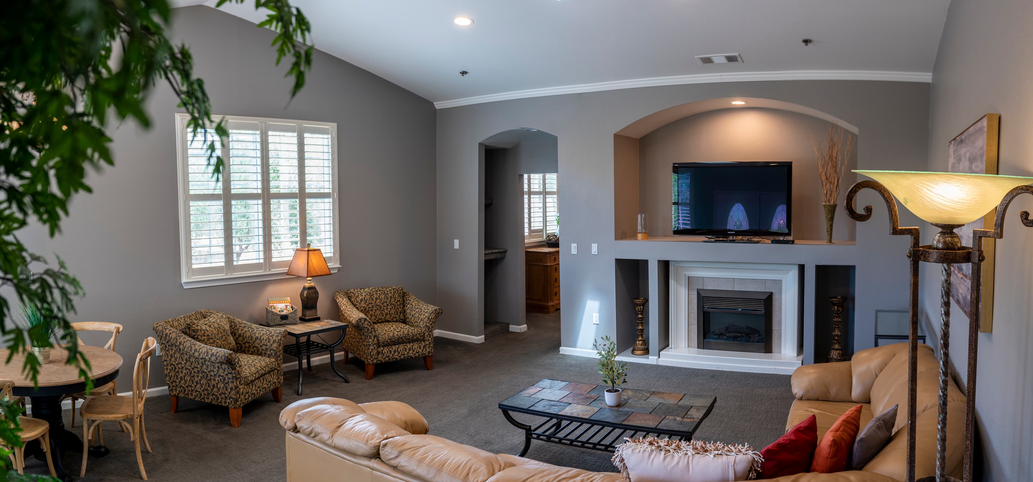 A panoramic view of a living room with a fireplace, a flat-screen TV, a dining table with chairs, and comfortable seating arrangements including a sofa and armchairs.