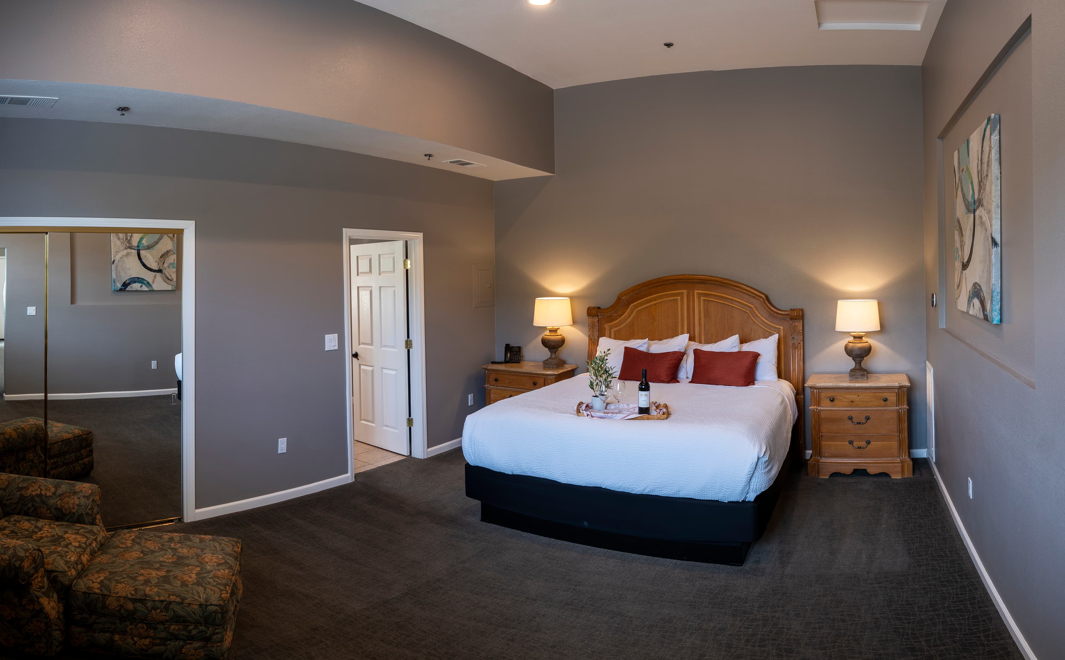A tranquil room with a king-size bed dressed in crisp white linens. Two nightstands with lamps flank the bed, and an armchair provides a cozy spot to relax.