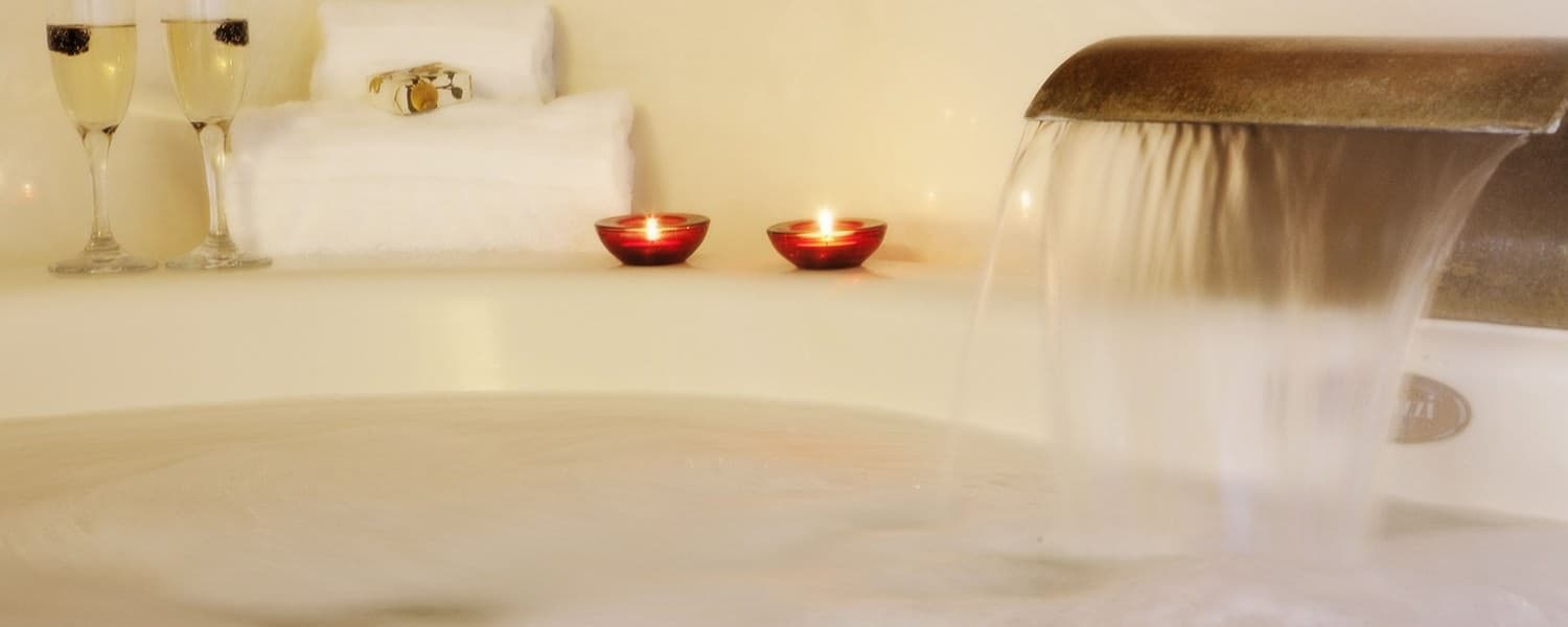 A luxurious Jacuzzi tub with water flowing from a spout. Two lit candles and a set of toiletries are placed on the side of the tub, creating a relaxing atmosphere.