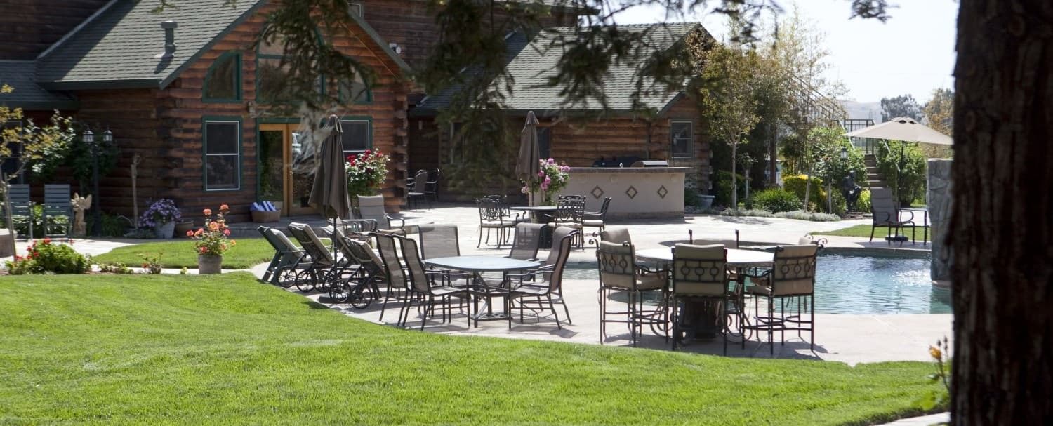 A view of a backyard with a swimming pool surrounded by lounge chairs and a dining table with chairs.