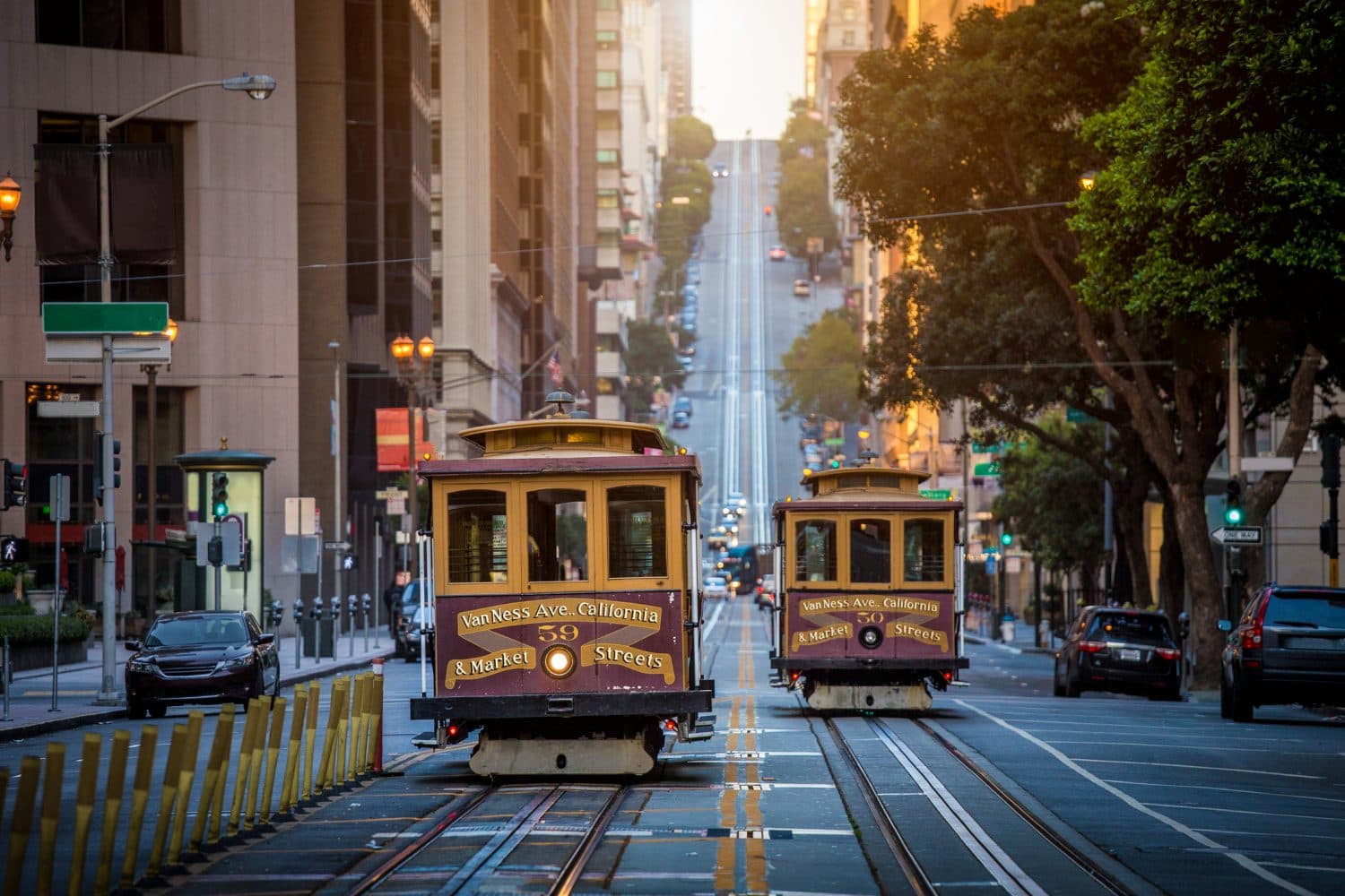Two vintage cable cars travel down a San Francisco street at sunrise.