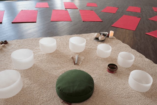 A serene space for meditation featuring circular bowls, a green cushion, and several red yoga mats arranged on the floor.