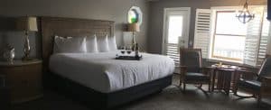 A modern hotel room featuring a large bed, two chairs, and a small table with drinks.