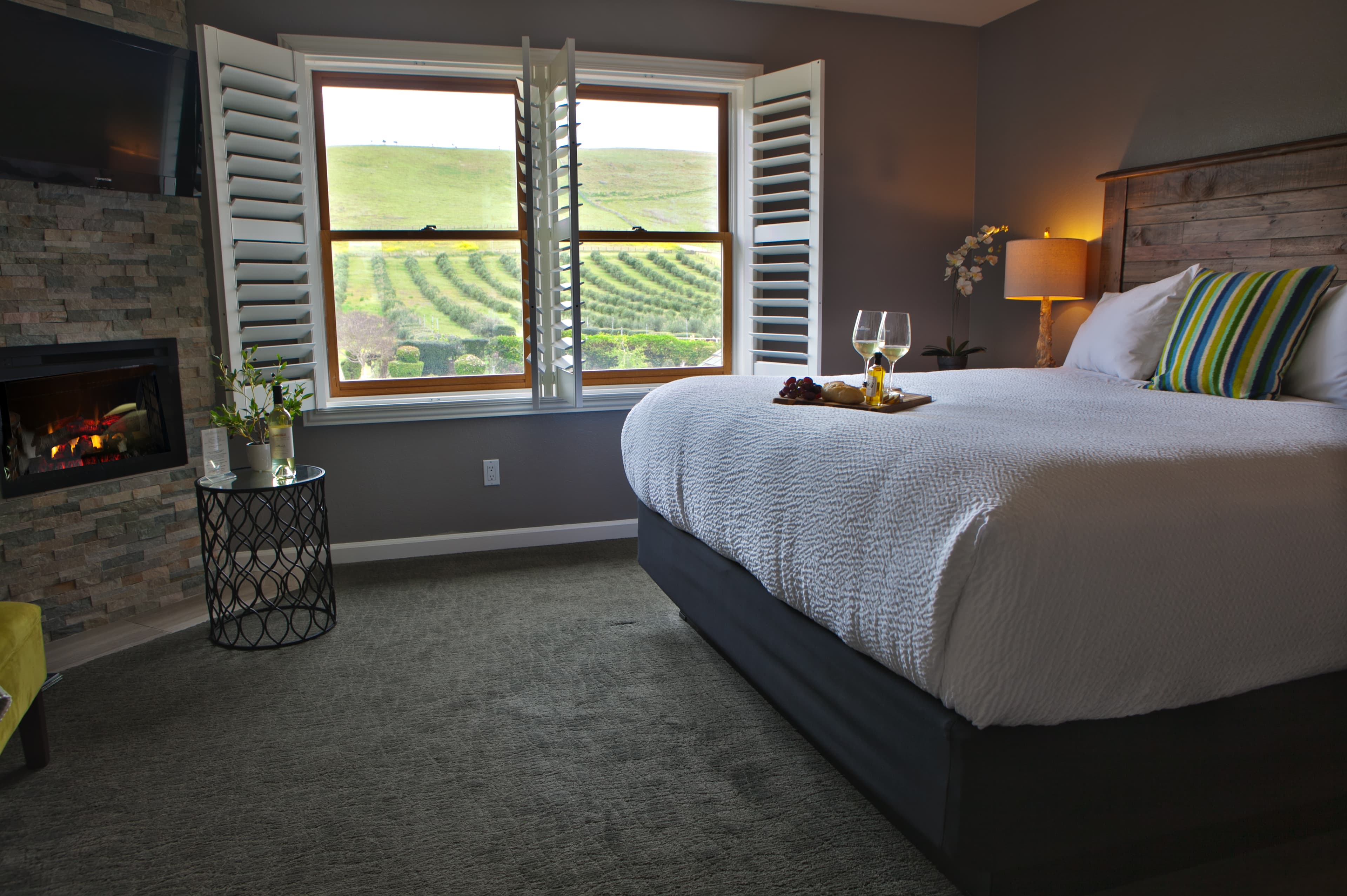 A cozy hotel room with a king-size bed and view of the olive orchard and pool area