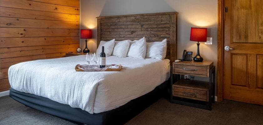 A cozy bedroom featuring a king-sized bed with white linens, wooden accents, and red lamps.