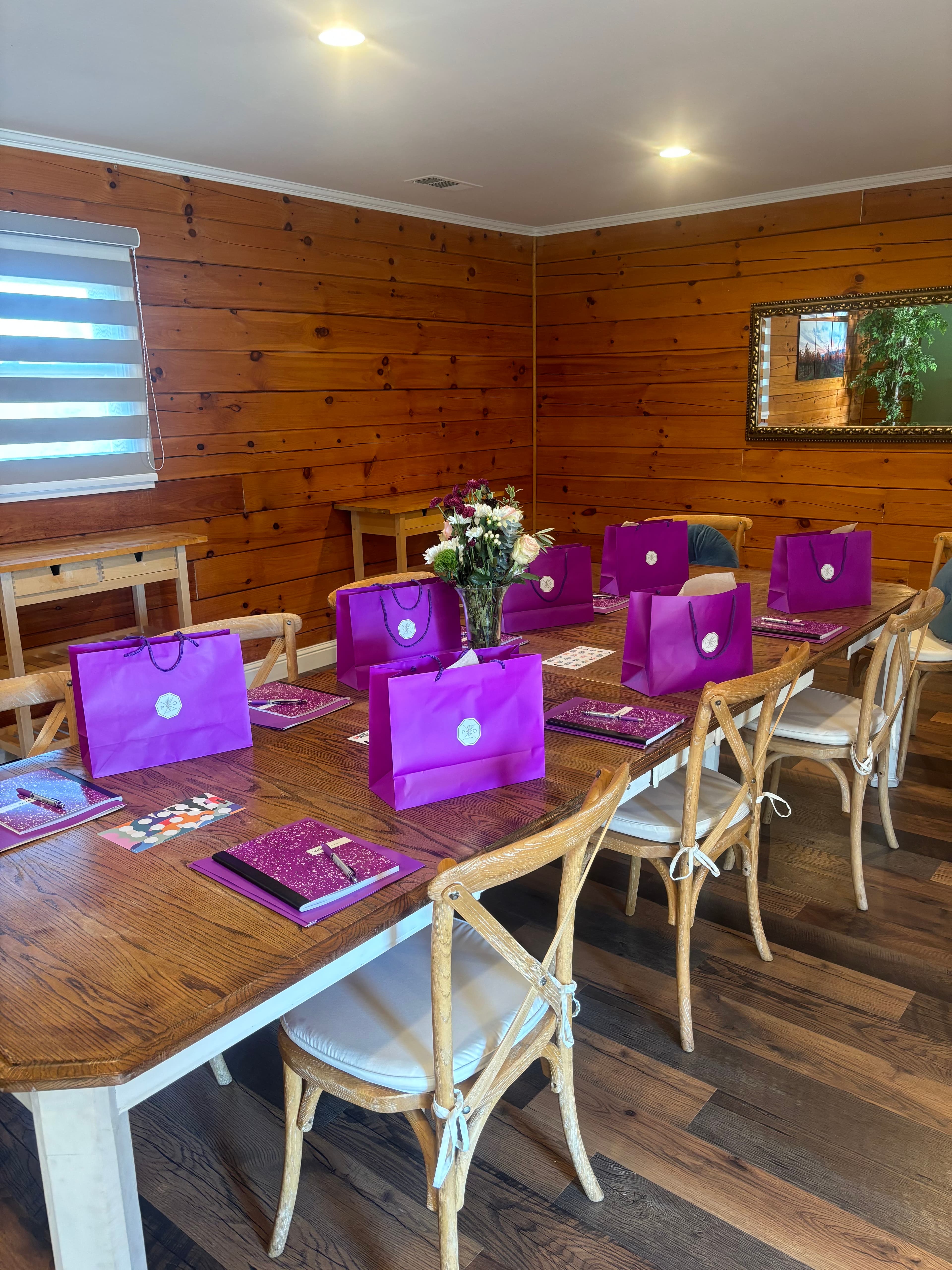 A dining table set with purple gift bags and floral arrangements in a cozy wooden room.