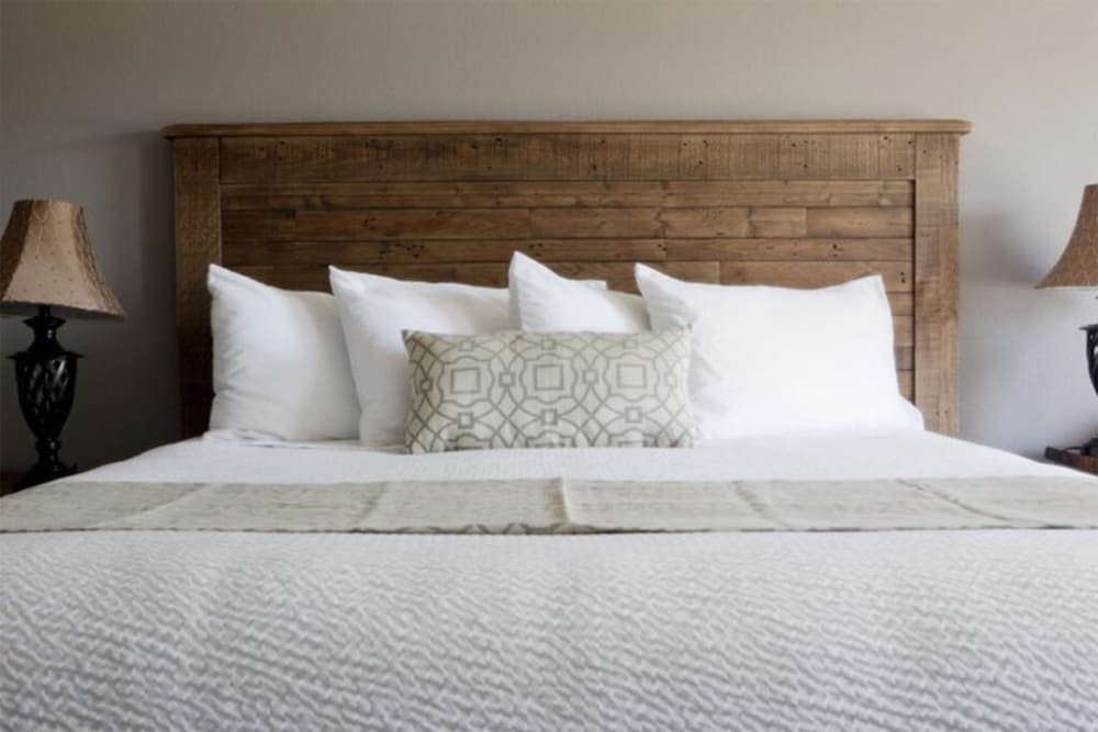 Bed with wood headboard, white coverlets, pillows and side table and lamp