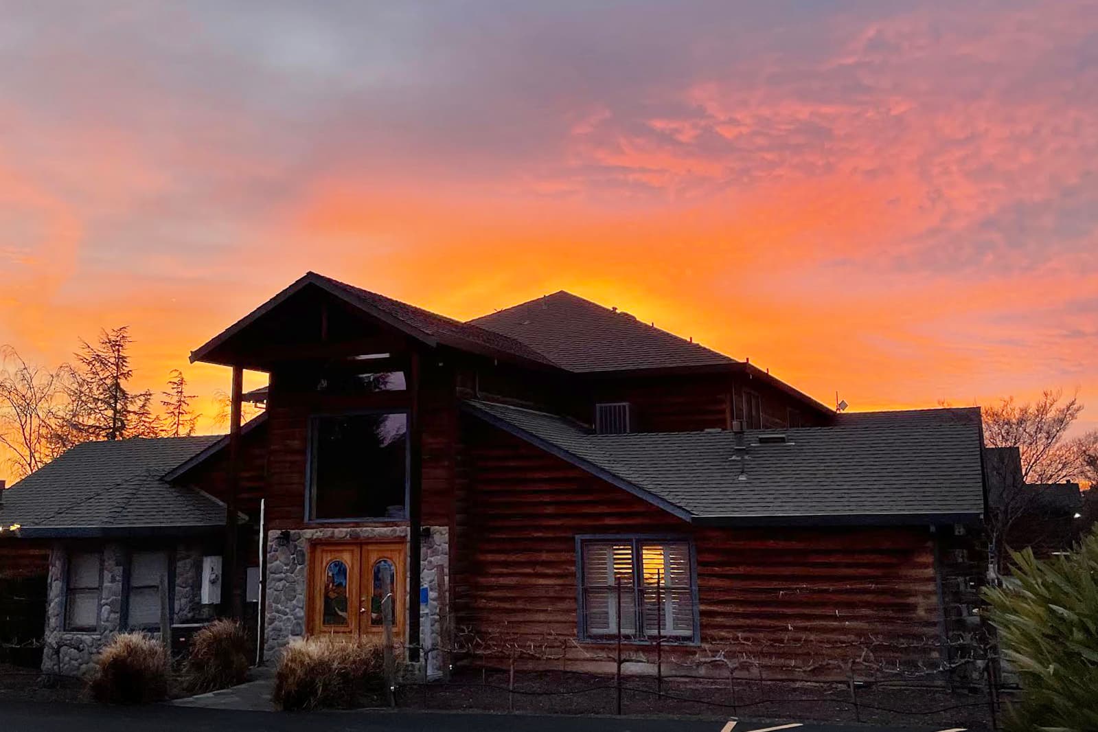A rustic building with wooden and stone features against a vibrant sunset sky.