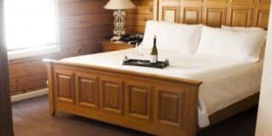 Cozy bedroom with a wooden bed, white linens, and a tray with wine.