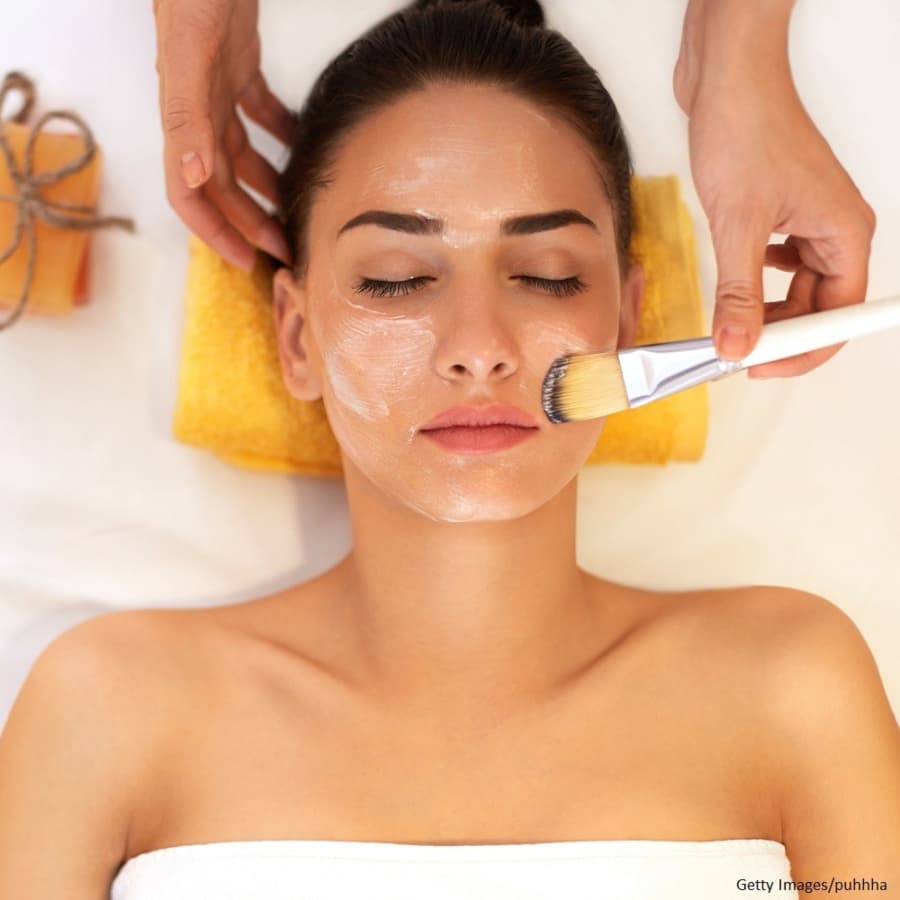 A woman receives a facial treatment while lying on a towel.