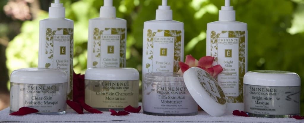 A collection of Eminence Organic Skin Care products displayed outdoors, showcasing various cleansers and moisturizers.