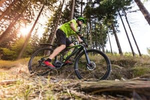A cyclist in a green shirt rides a mountain bike through a forest trail at sunset.