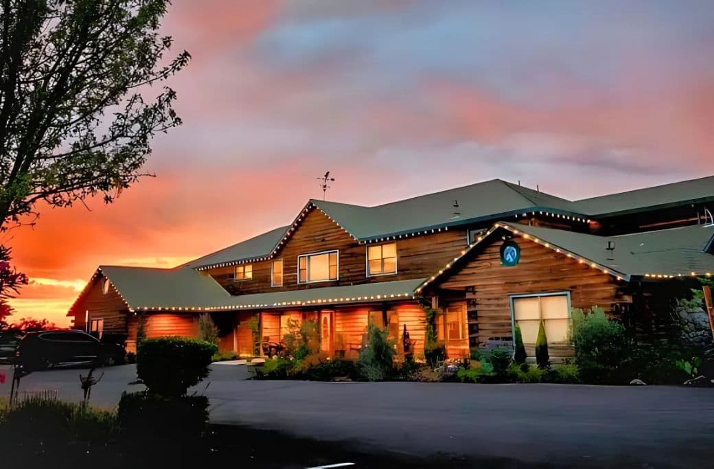A rustic wooden cabin lit by warm lights against a vibrant sunset sky.