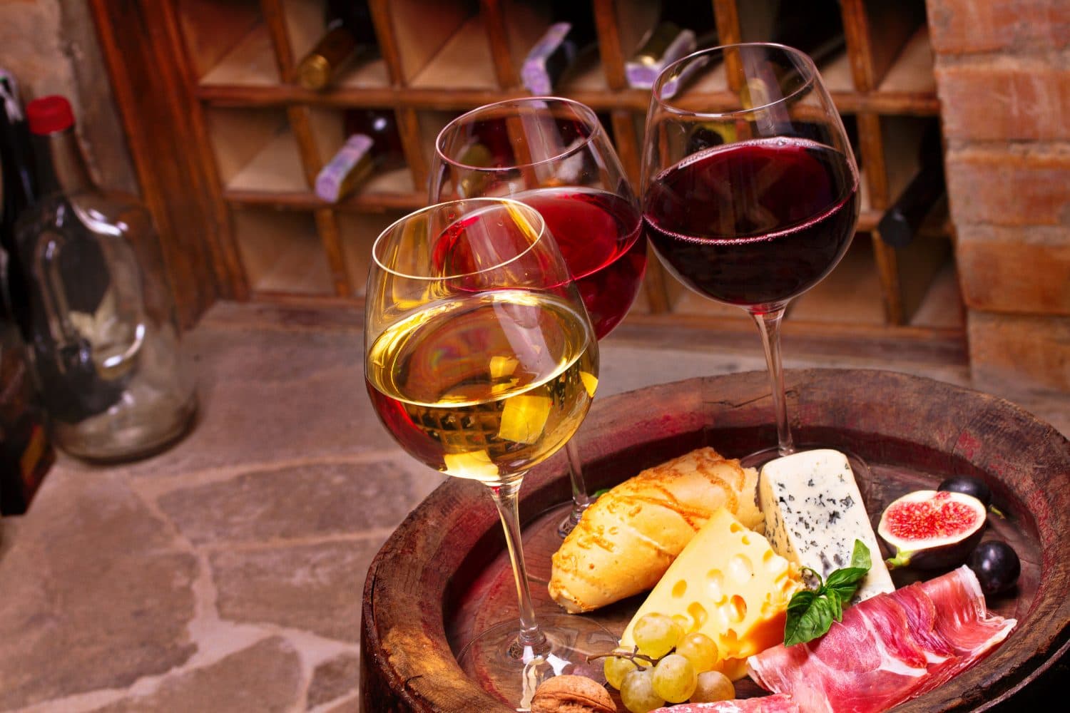 A selection of red and white wines accompanied by various cheeses, meats, and fruits on a wooden platter.