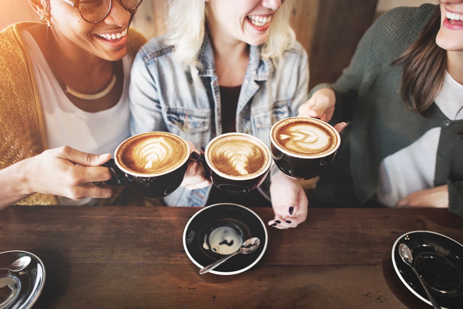 Three friends clink coffee cups with latte art while enjoying a cheerful moment together at a café. Three friends clink coffee cups with latte art while enjoying a cheerful moment together at a café.