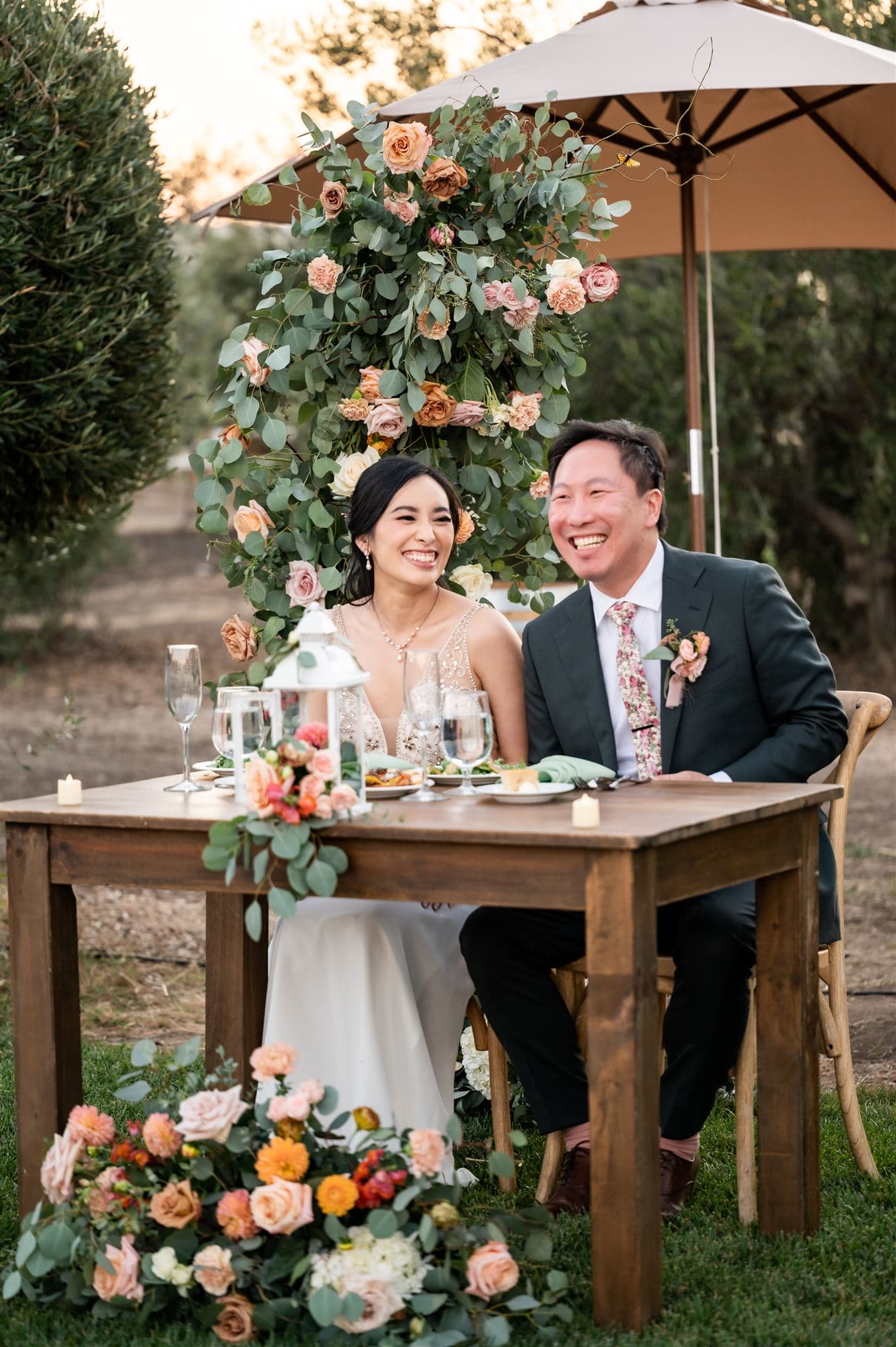 A smiling couple enjoys a romantic dinner at a beautifully decorated outdoor table surrounded by flowers.