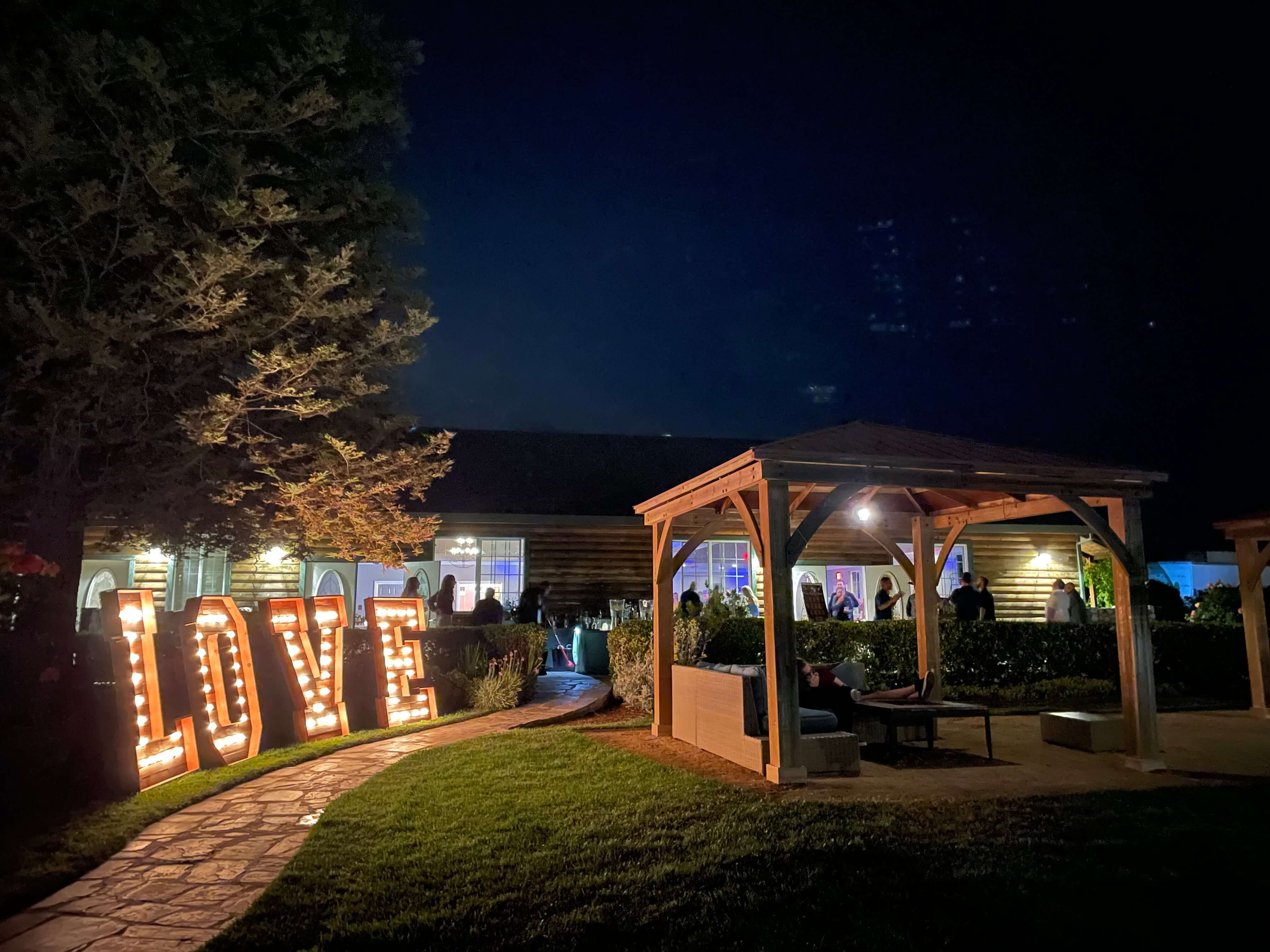 A garden area at night featuring illuminated "LOVE" letters and a wooden pavilion.