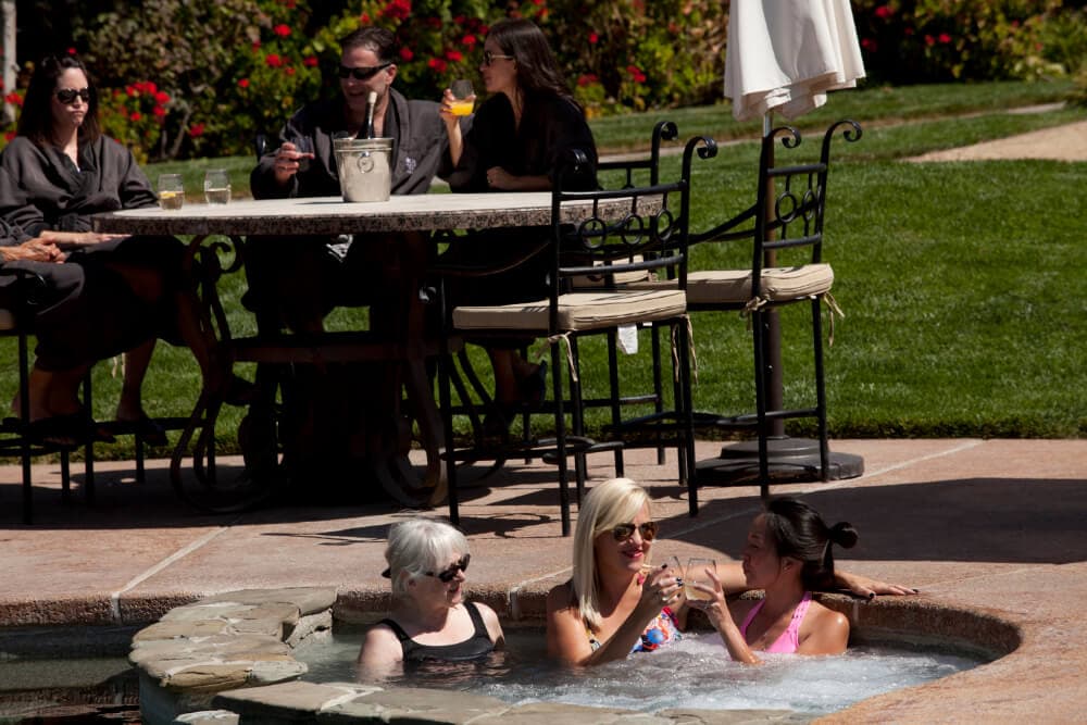 People relax by a pool, enjoying drinks and conversation in a sunny setting.