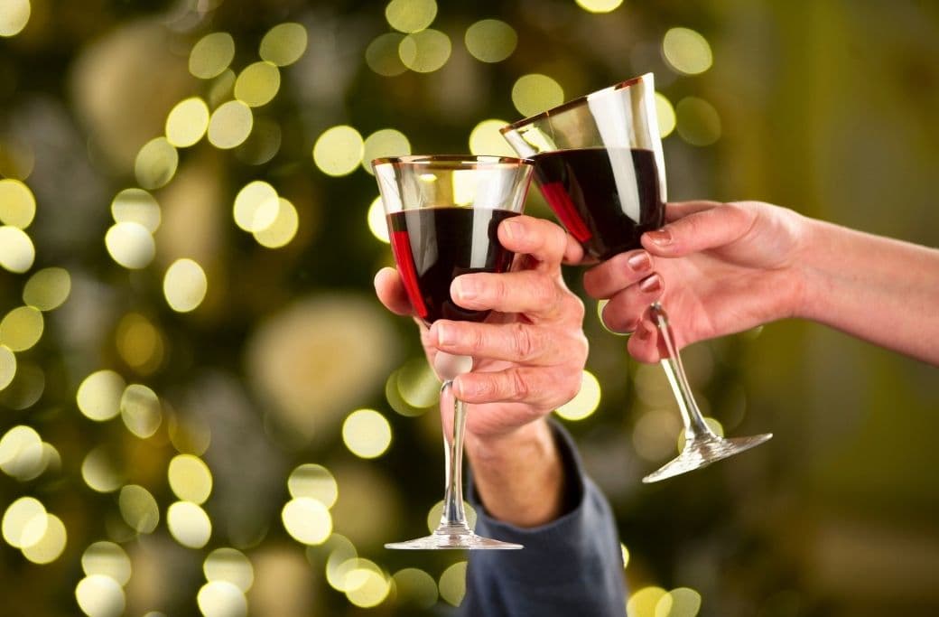 Cheers with two glasses of red wine against a festive, blurred background.