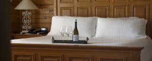 A cozy bedroom with a wooden bed, two wine glasses, and a bottle of wine on a tray.