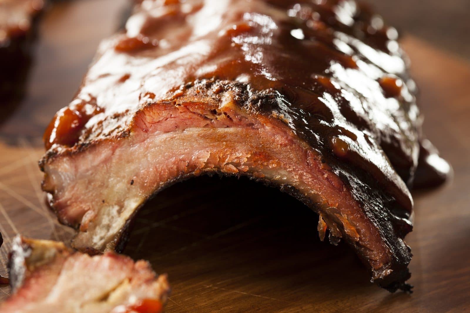 Close-up of succulent barbecue ribs coated in a glossy sauce, resting on a wooden cutting board. Close-up of succulent barbecue ribs coated in a glossy sauce, resting on a wooden cutting board.
