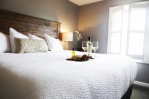 A cozy bedroom featuring a large bed, decorative pillows, and a small table with wine and glasses.