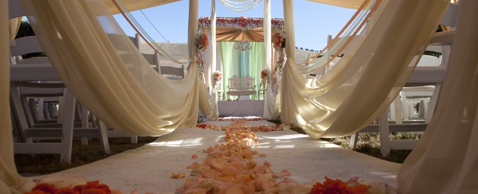 An elegantly decorated outdoor wedding aisle lined with flower petals and draped fabric.