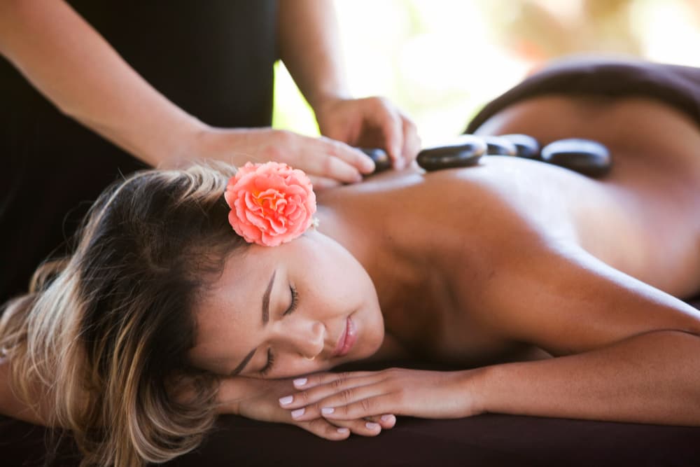 A woman receives a hot stone massage outdoors, with a flower in her hair.