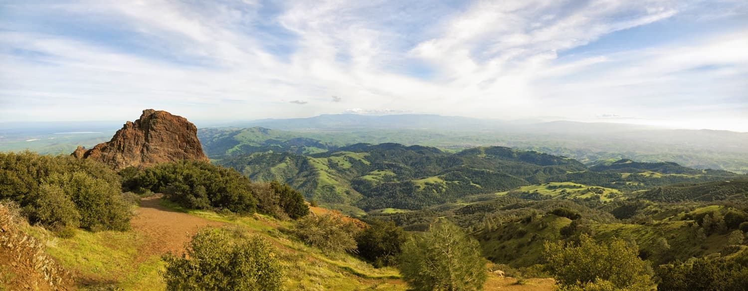 Panoramic view of lush green hills and a rocky outcrop under a partly cloudy sky. Panoramic view of lush green hills and a rocky outcrop under a partly cloudy sky.