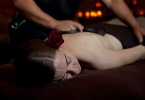 A woman is receiving a massage while adorned with a rose in her hair.