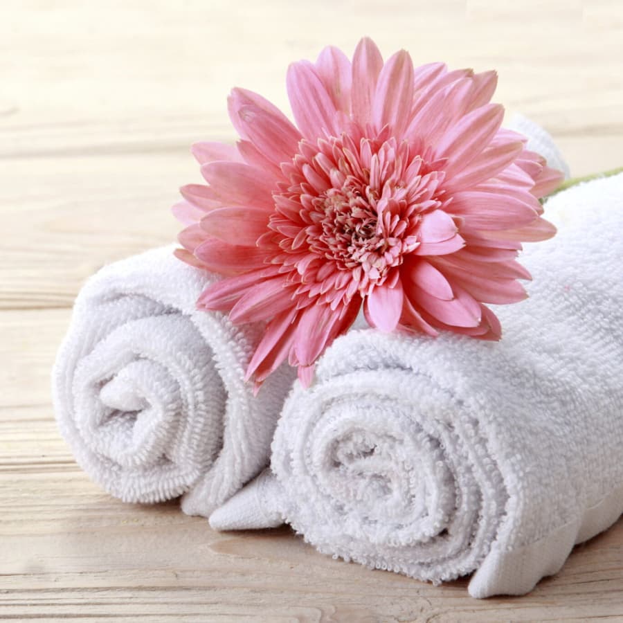 Two rolled white towels accompanied by a pink flower on a wooden surface.