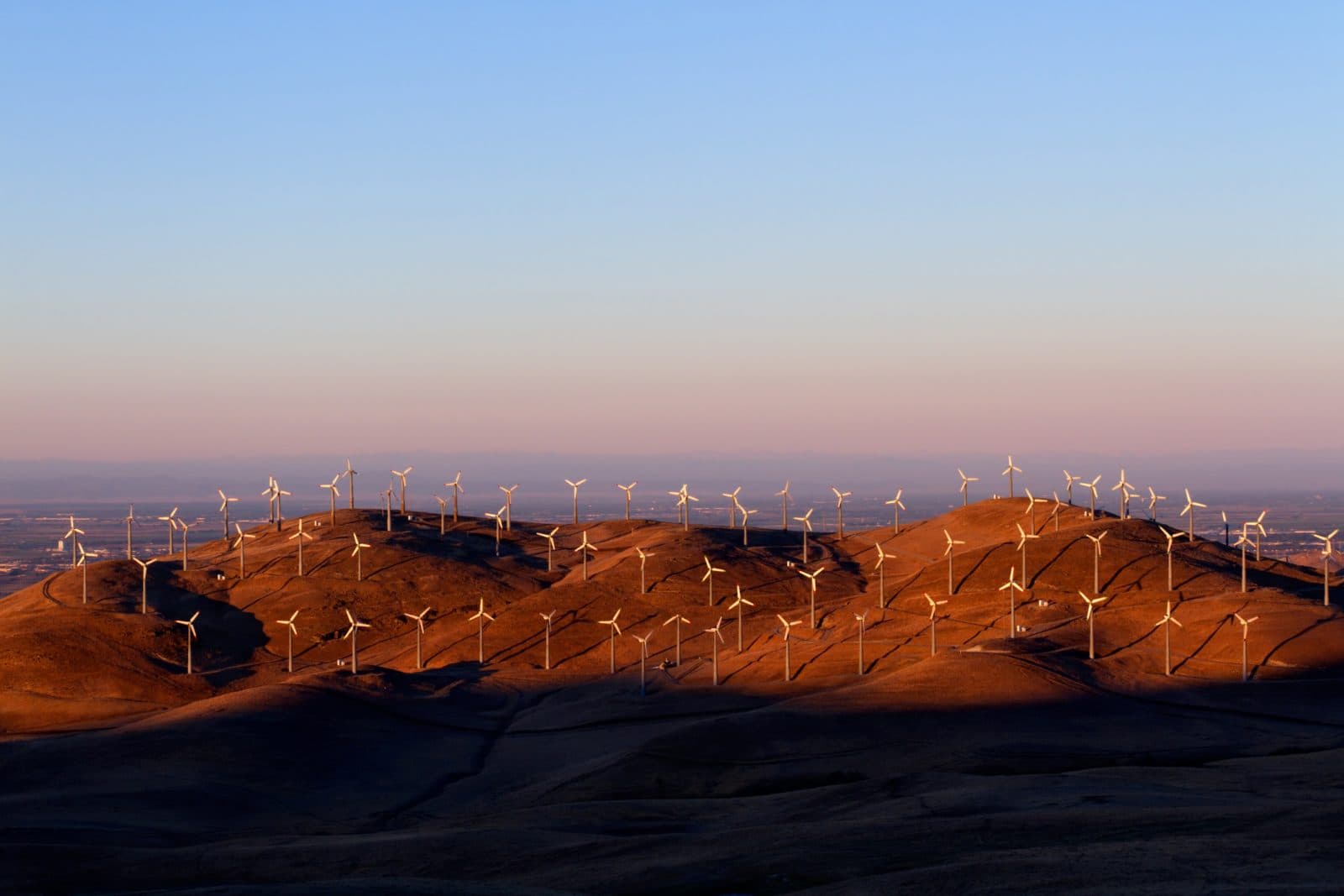 Wind turbines line the hills at sunset, casting long shadows over the landscape. Wind turbines line the hills at sunset, casting long shadows over the landscape.