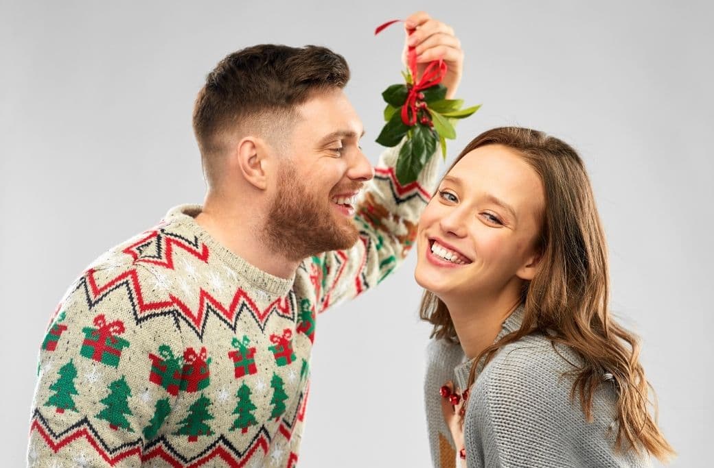 A smiling couple poses under mistletoe, with the man playfully attempting to kiss the woman. A smiling couple poses under mistletoe, with the man playfully attempting to kiss the woman.