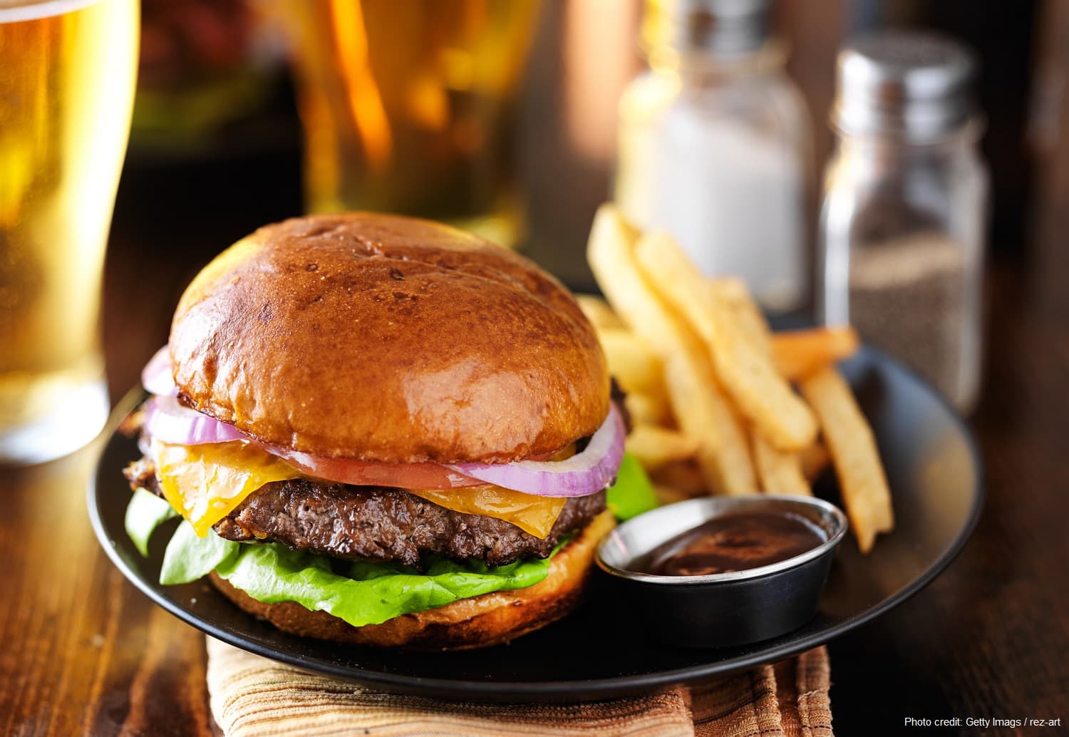 A juicy cheeseburger with lettuce, onion, and fries on a black plate.