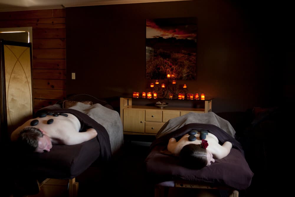 Two people receiving massages with heated stones in a dimly lit spa setting.